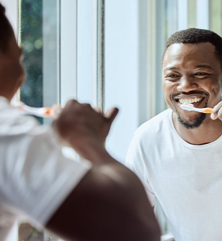 Man smiling while brushing his teeth in bathroom