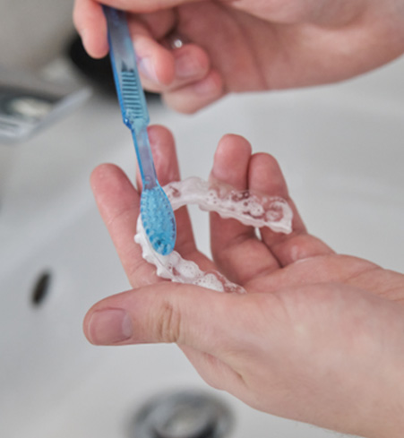 Patient cleaning clear aligner in sink