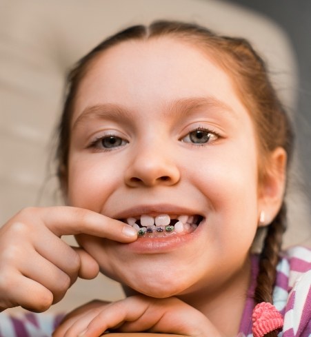 Child receiving phase one pediatric orthodontics pointing to smile