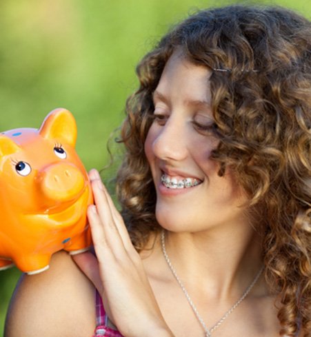 woman with braces looking and smiling at an orange piggy bank