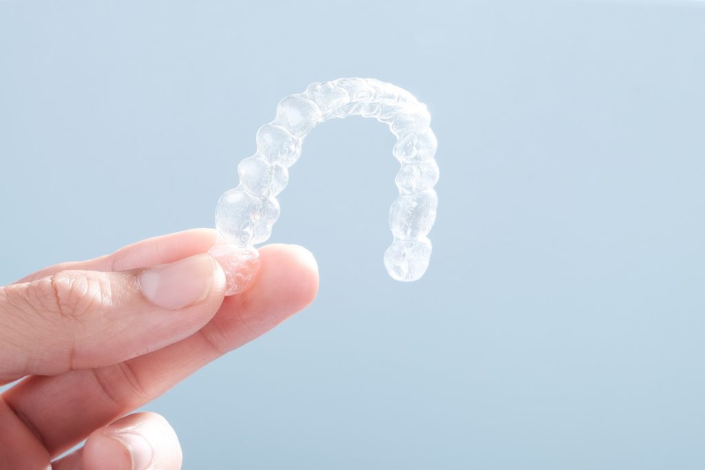 Closeup of patient holding clear aligners on blue background